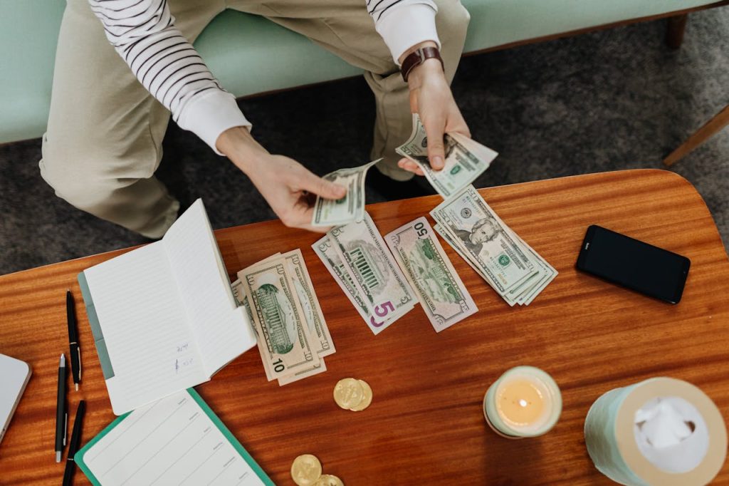 pexels-photo-6328948 A person sitting and counting various US dollar bills at a table indoors.
