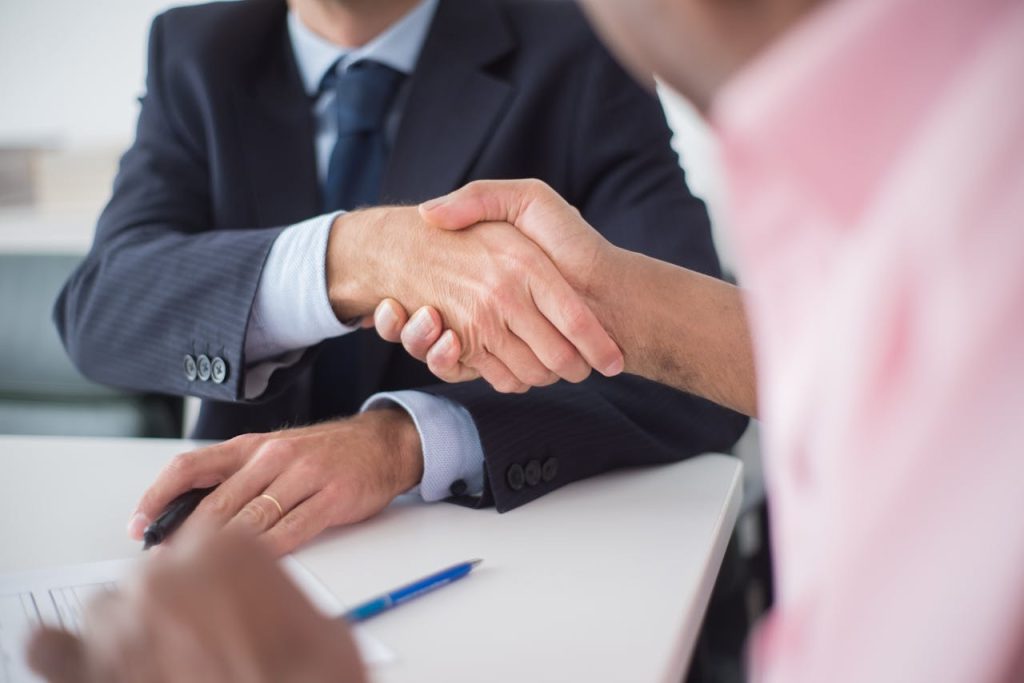 pexels-photo-8441790 Two businessmen shaking hands across table, symbolizing agreement and partnership in an office environment.